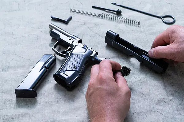 disassembled handgun spread on a table with hands cleaning the parts