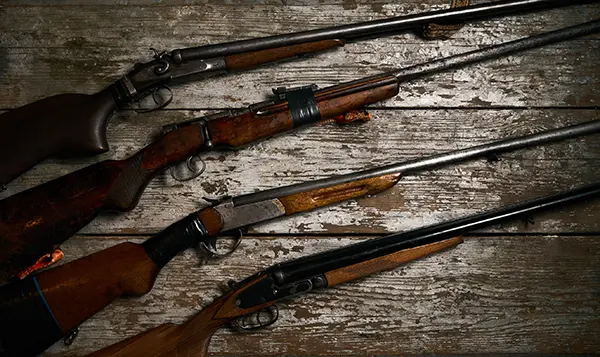 four rifles laying horizontally on a worn wooden background